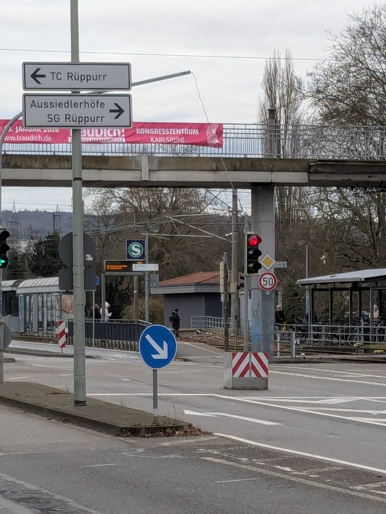 Foto von der Herrenalber Straße mit Blick auf die Haltestelle Battstraße. In der Bildmitte ist eine Behelfsampel zu sehen, die auf einem großen Betonblock montiert ist. Aufgestellt ist er zwischen der Linksabbieger Spur und Geradeaus Spur.
