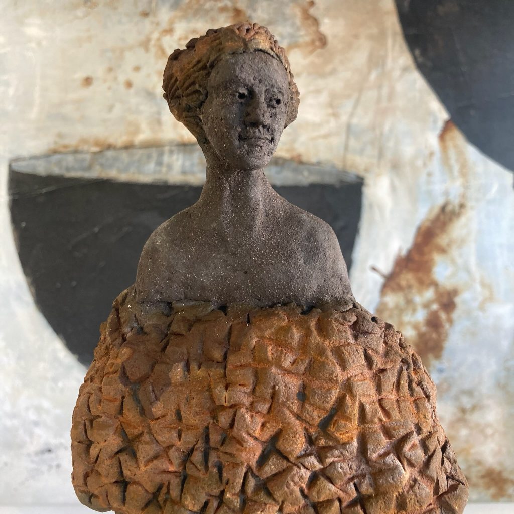 Foto einer Ton Figur einer Frau der Künstlering Luiza Noss.
Im Hintergrund ist ein Gemälde zu sehen. Die Künstlerin verbindet damit das Bild mit der Figur.