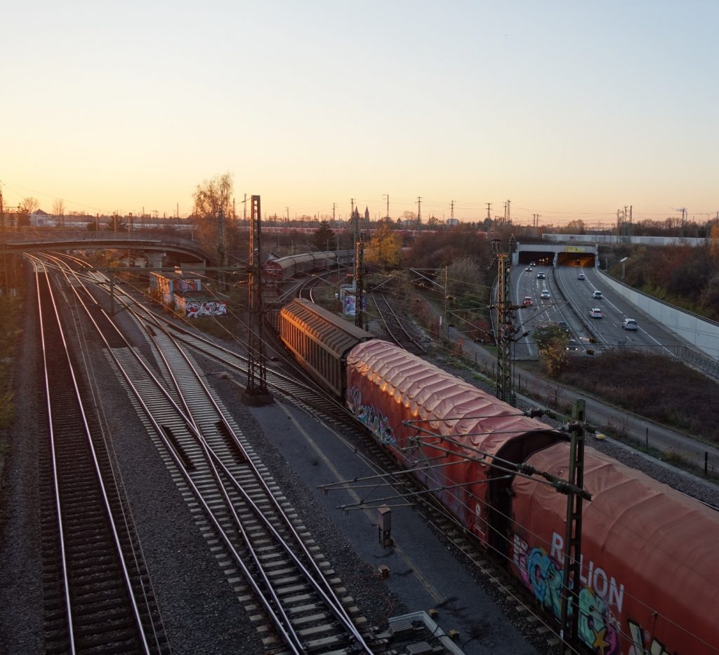 Foto aufgenommen von der Weiherfeldbrücke Richtung Westen. Abendstimmung mit Sonnenuntergang. Sicht auf die Gütergleise und die Südtangende. Es ist ein Güterzug zu sehen.