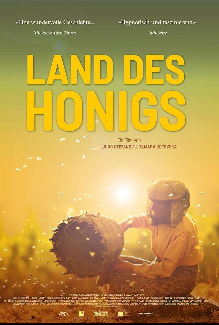 Poster des Films Land des Honigs.
Der verschwommene Hintergrund läuft von oben grün nach unten in ein warmes gelb.
In der Mitte ist ein Imker zu sehen, der einen runden Bienenstock in der Hand hält.