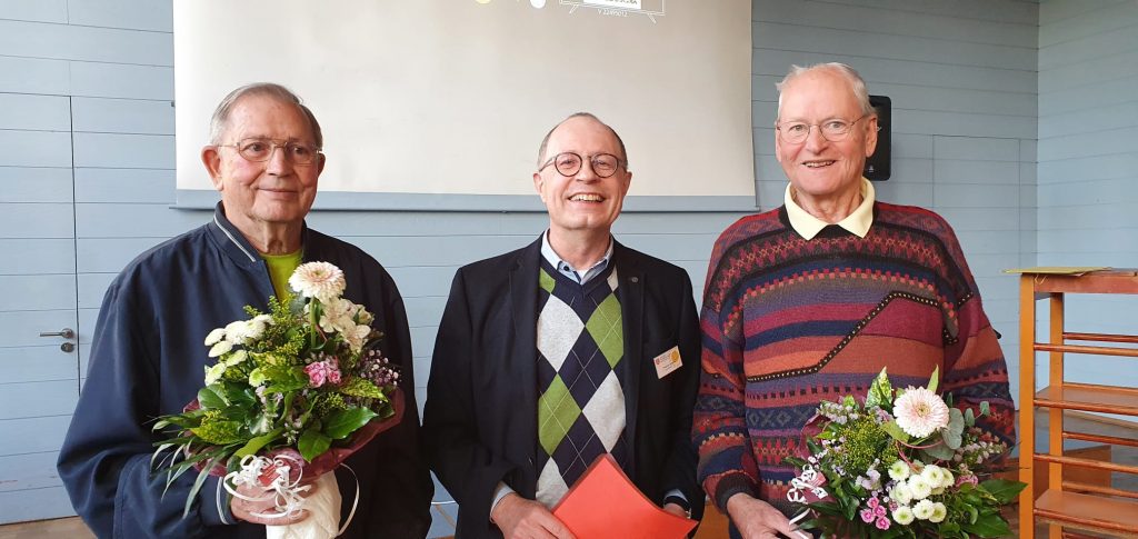 Aufnahme der Überreichung von Blumenstraußen an zwei der 50 Jahre Mitgliedschaft Jubilare. Drei Männer sind zu sehen die in die Kamera schauen. Beide Jubilare haben einen großen Blumenstrauß in der Hand.